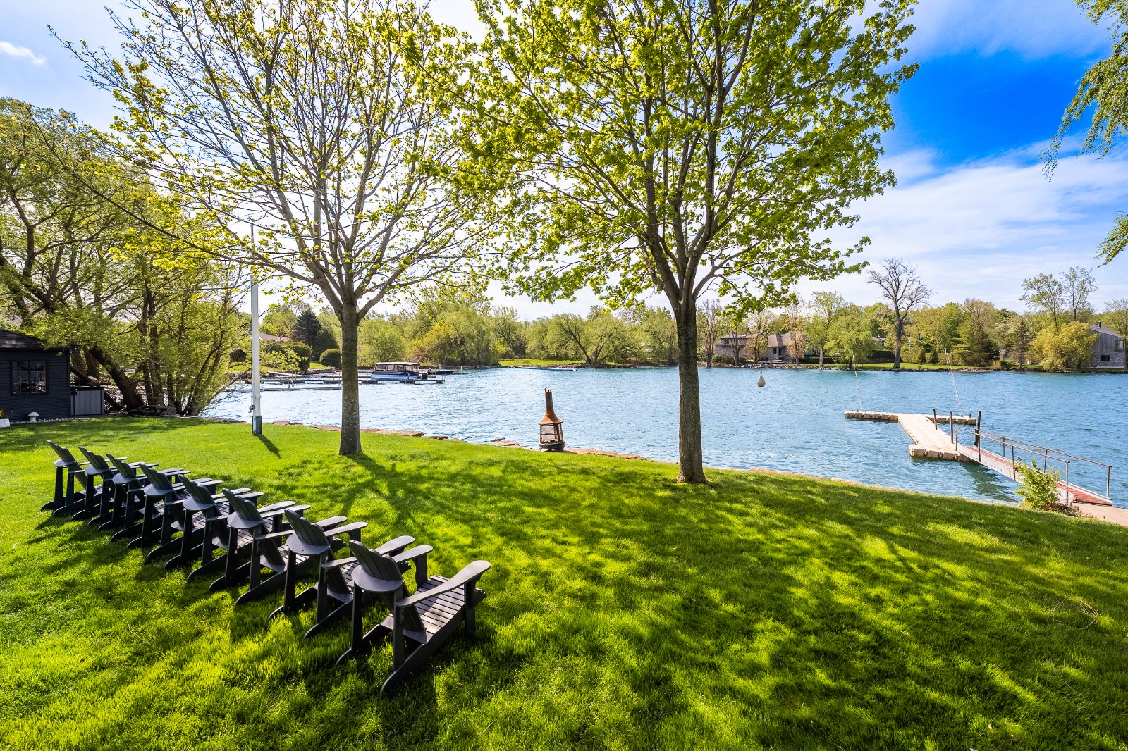 Waterfront lawn with Adirondack chairs, mature trees and a dock on Lake Saint-Louis